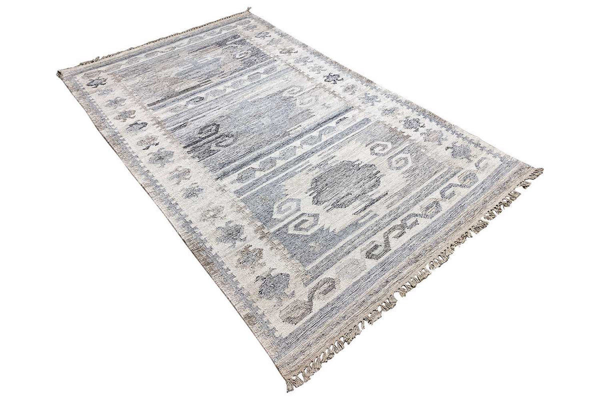 Kilim dhurrie rug viewed at an angle, with geometric motifs and a light gray-blue color scheme