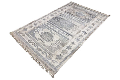 Dhurrie rug viewed from above at an angle, with ornamental stripes, light gray-blue, and fringe