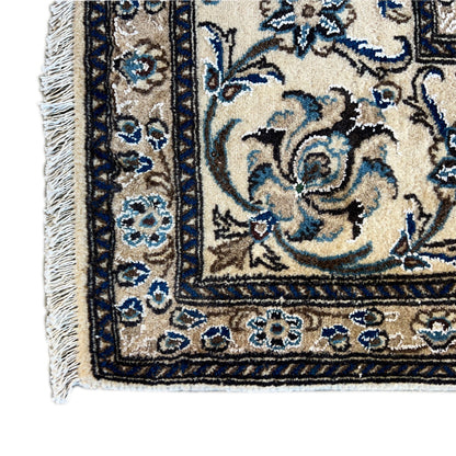 Close-up of a rug edge with fringes: beige background, blue vine ornaments, and border