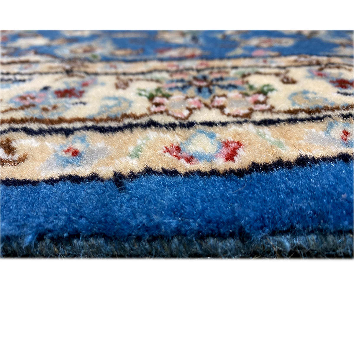 Edge detail of a blue Nain rug with a colorful pattern and dense pile.