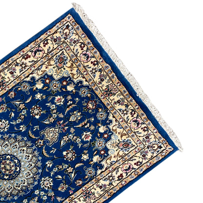 Corner of a blue Nain rug with a border pattern and fringed edging.