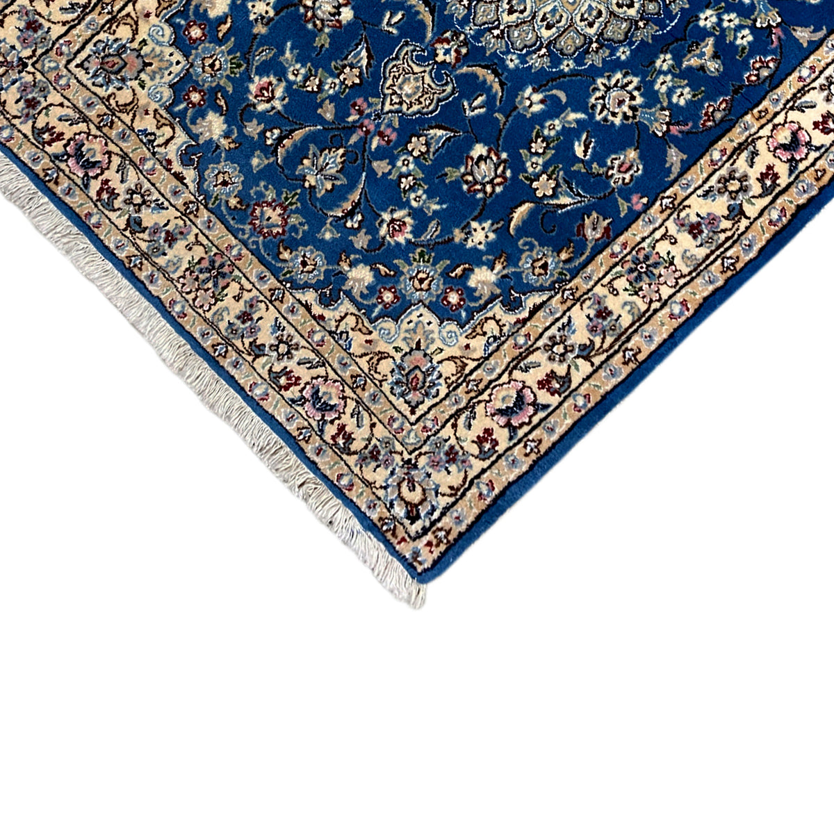 Corner of a blue Nain rug with a floral border and fringes at the tip.