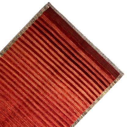 Rug from the side: reddish-brown stripes and a beige border with a bound edge