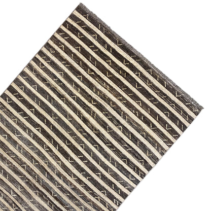 Rug viewed at an angle with brown-black stripes, a pattern, and fringes along the edge