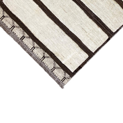Corner of the Nimbaft rug with brown stripes and an embroidered decorative fringe border