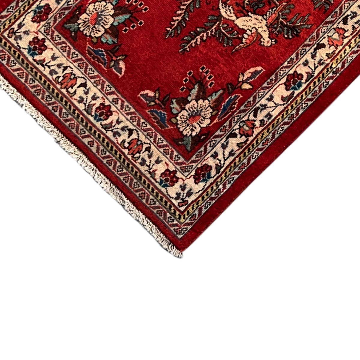 Corner of a red rug with colorful borders, ornaments, and short fringe trim