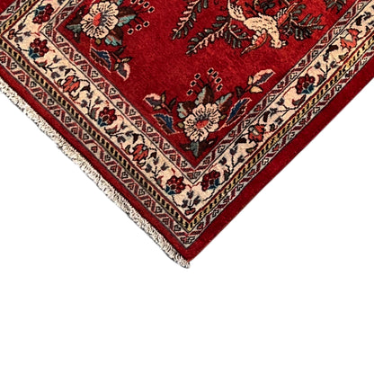 Corner of a red rug with colorful borders, ornaments, and short fringe trim
