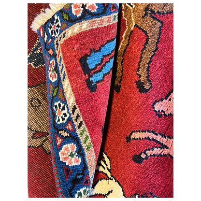 Wool rug edge view: blue multicolored border, red field with animal motif