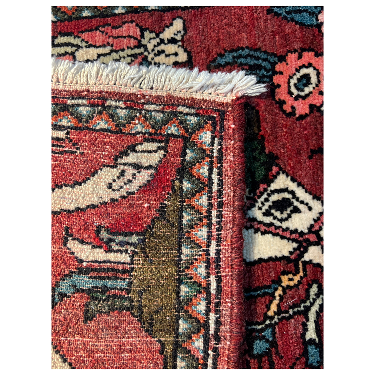 Detail of the carpet edge with fringes and colorful ornaments on a red patterned section