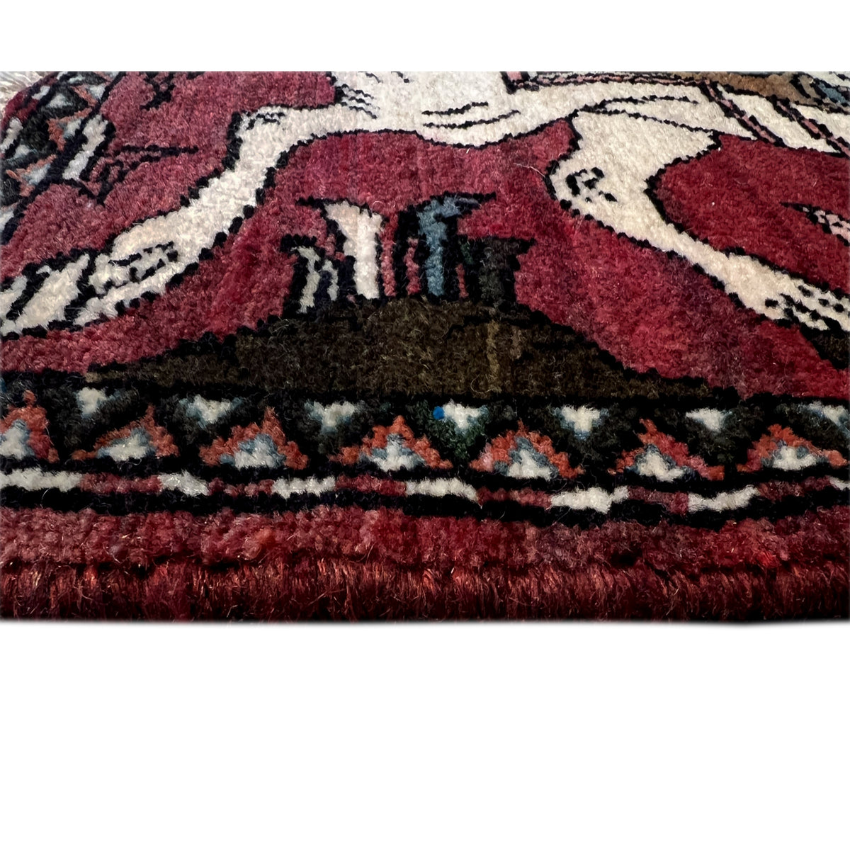 Bottom edge of a red Hamedan rug with a woven pattern and fringed trim