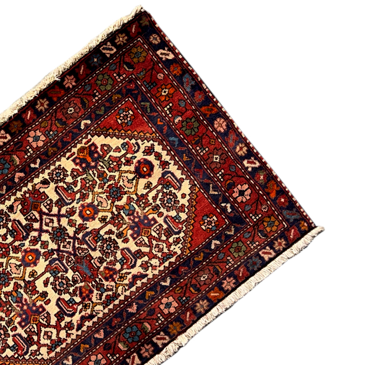 Corner of a rug with a red background, detailed border pattern, and light-colored fringes