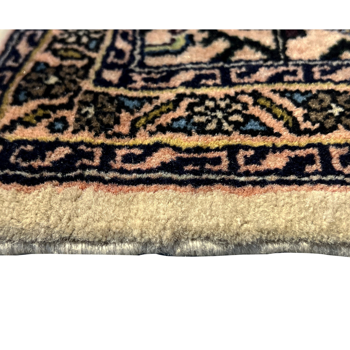 Fabric detail at the edge: beige Poshti rug with a dense ornamental border and fringed trim