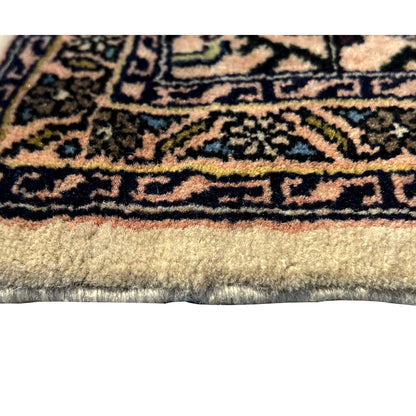 Fabric detail at the edge: beige Poshti rug with a dense ornamental border and fringed trim