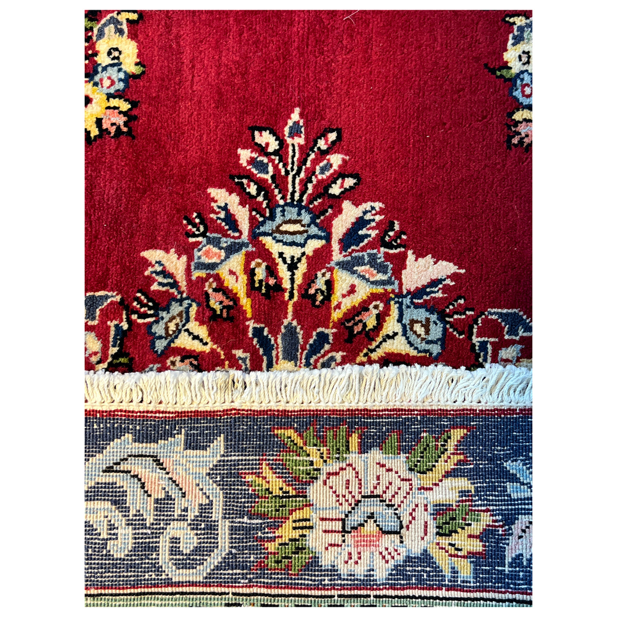 Close-up of carpet pile: red field with blue and yellow ornaments, fringes