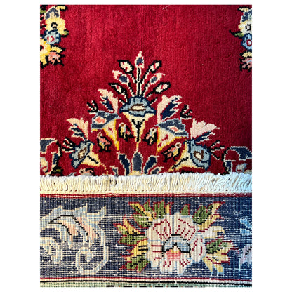 Close-up of carpet pile: red field with blue and yellow ornaments, fringes
