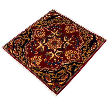 Square rug with a red patterned center and dark blue vines, edged with fringes