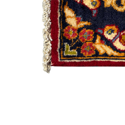 Corner detail of a fringed carpet with ornamental patterns in red, dark blue and gold