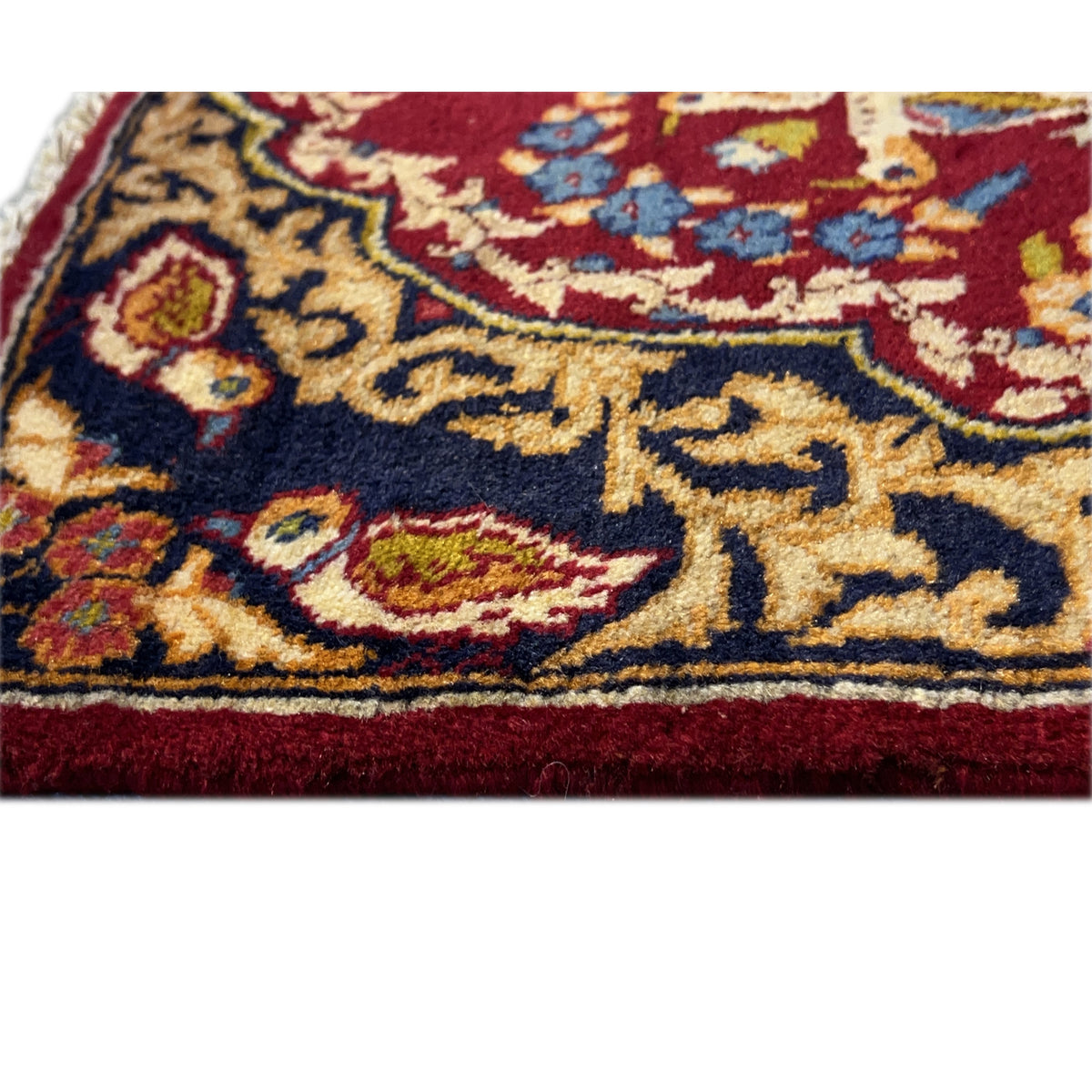 Close-up of a carpet edge: dark blue background with golden vines, red border, fine texture