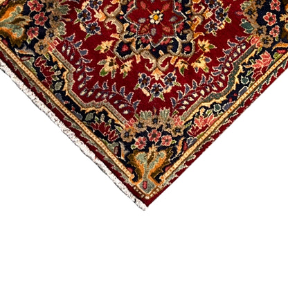 Diagonal corner view: red rug with ornaments and a white fringed edge along the border