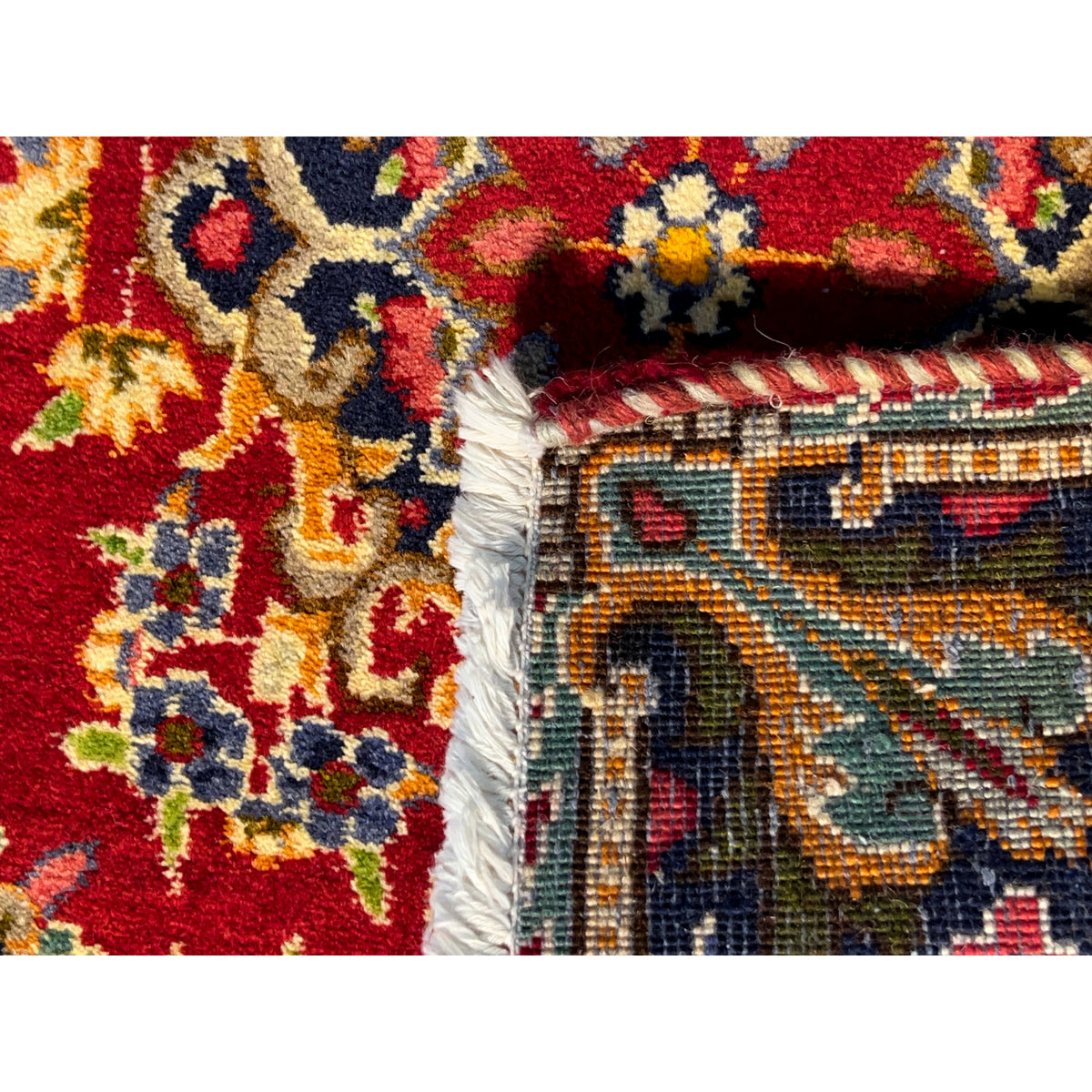 Close-up of the side edge of a rug: red pattern, bound border, and fringe