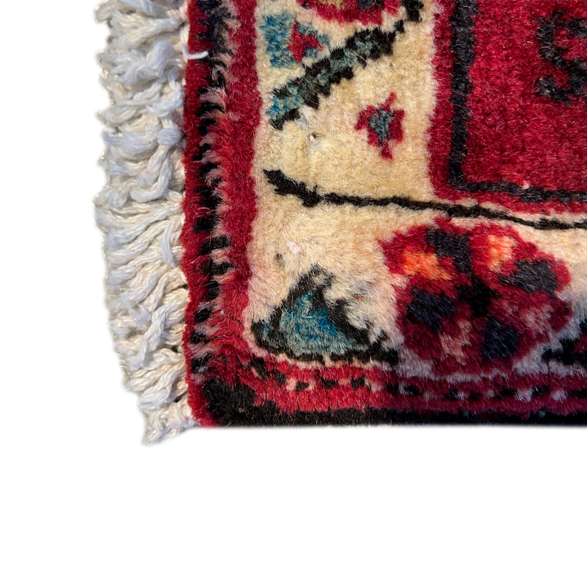 Edge detail with white fringes on the red Poshti rug and colorful border
