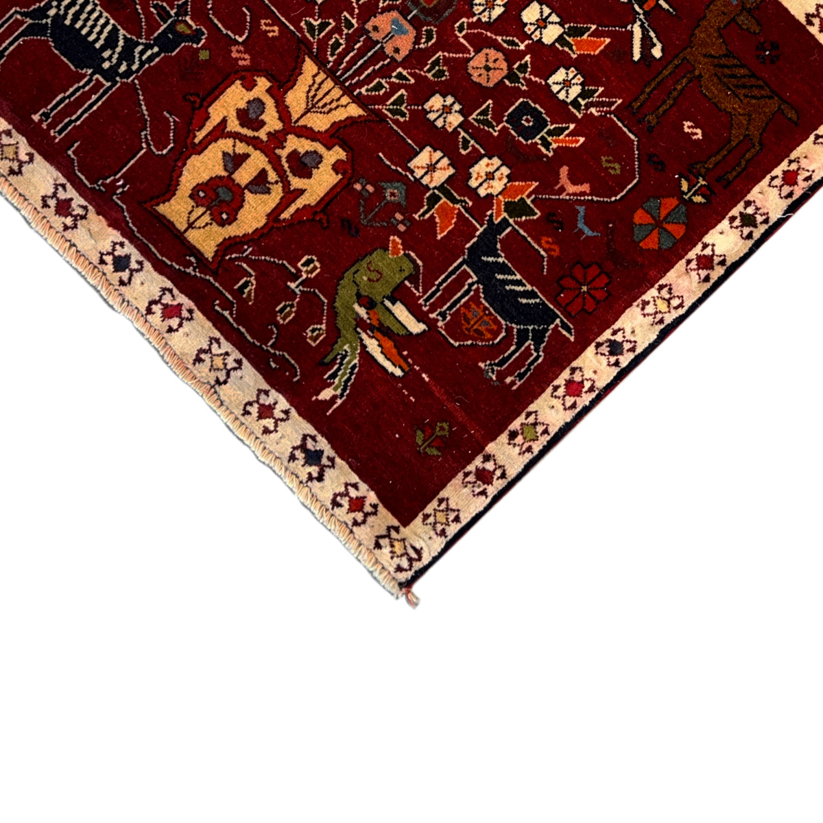 Corner of the red Poshti rug with a border pattern, colorful figures, and short fringes