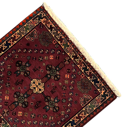 Close-up of a red Poshti rug: geometric border, intricate patterns, and fringe along the edge