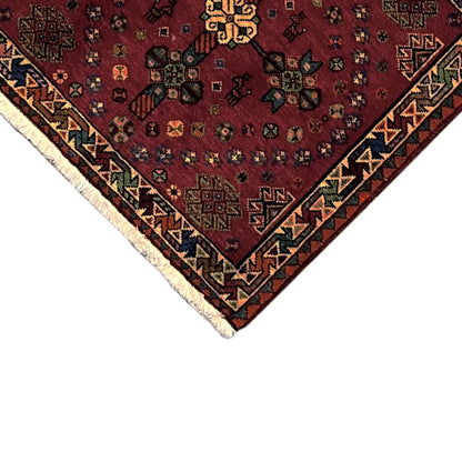 Red Poshti rug in a corner: multicolored decorative border, fringe, and dense pattern