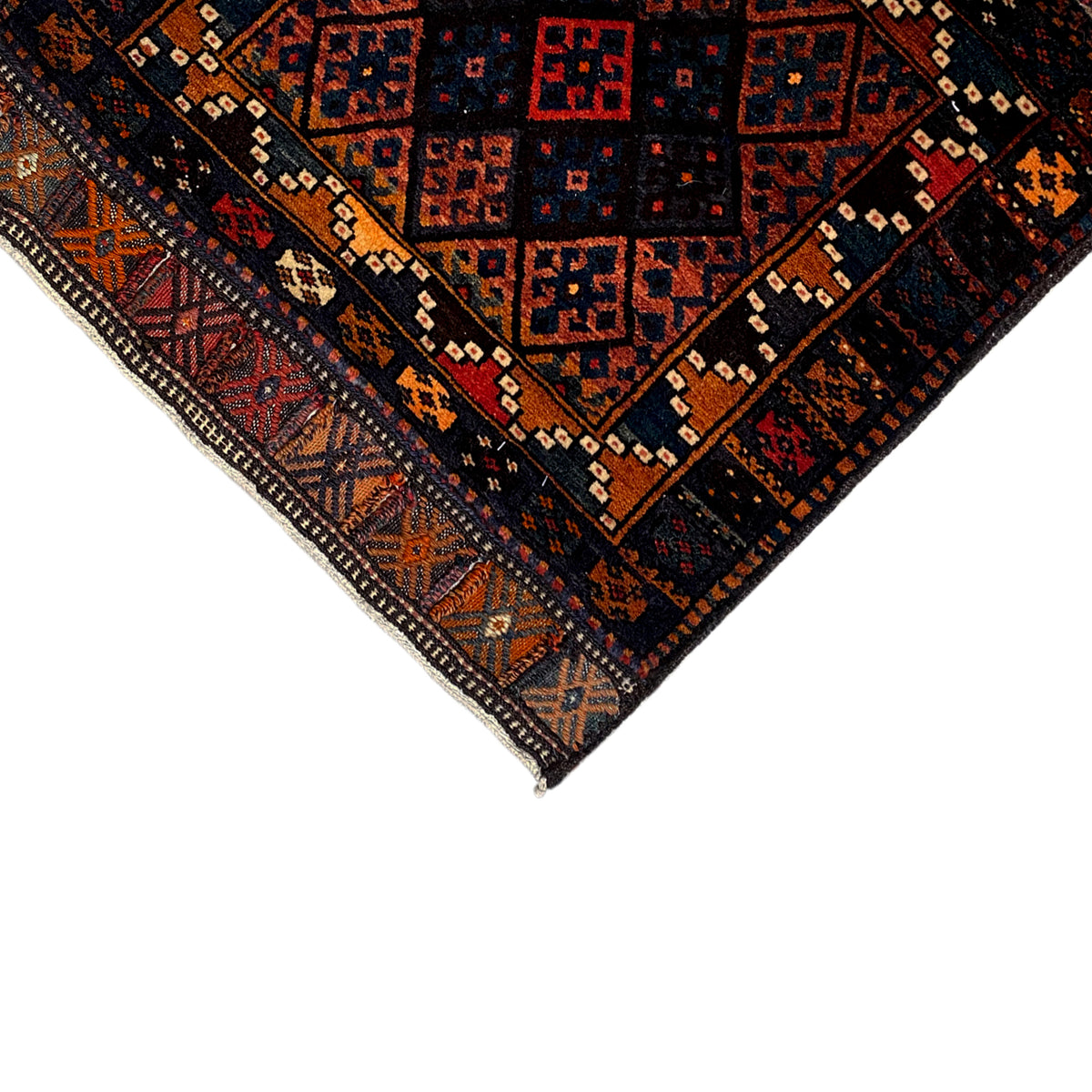 Rug corner with a dark pattern, border, and fringed edges, with red and orange accents