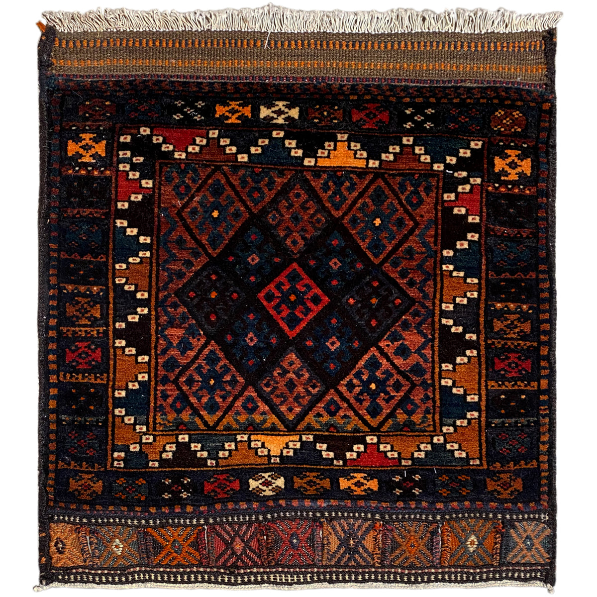Rug with a dark background, geometric pattern in shades of red, blue, and orange, fringes