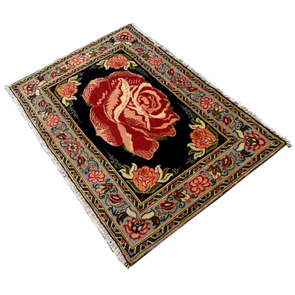 Hamedan Poshti rug at an angle, black background with red rose motifs in the medallion.