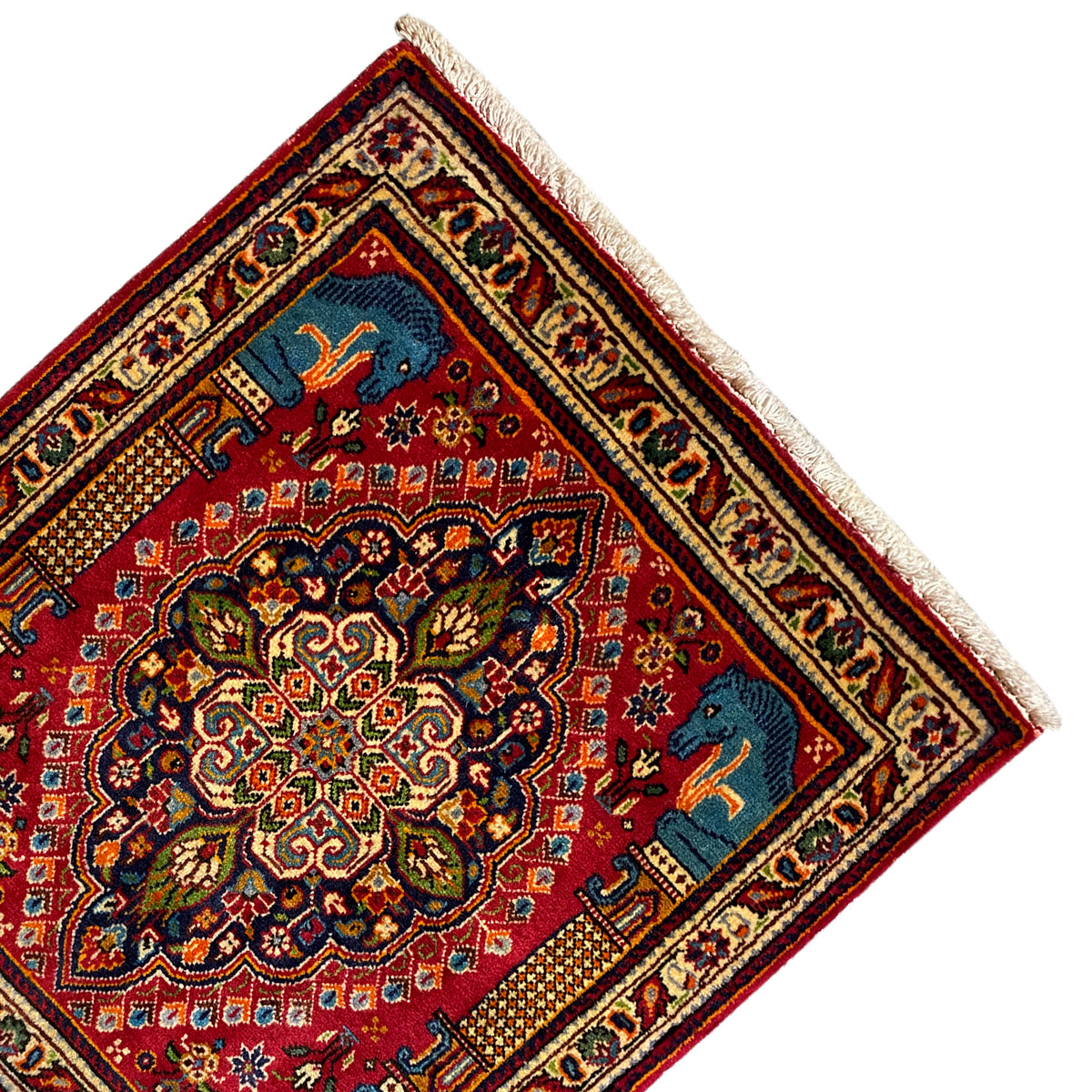 Rug at an angle: red central ornament, blue animal motifs in the corners, cream border