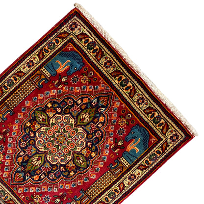 Rug at an angle: red central ornament, blue animal motifs in the corners, cream border