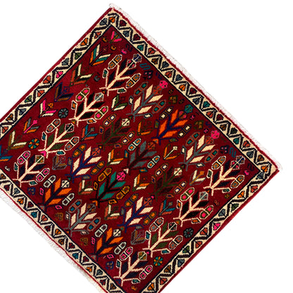 Rug at an angle: red field with rows of trees, framed border, and fine fringes.