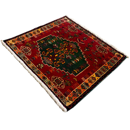 Red rug with a dark border, green center, patterned sides, and fringes