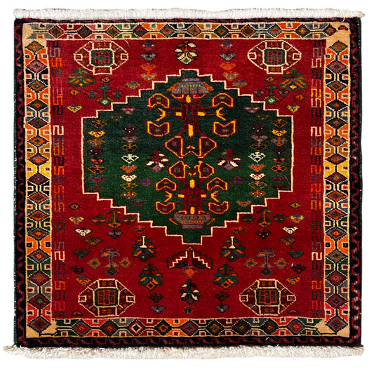 Rug with a red background and green/yellow ornaments, with a white fringed edge
