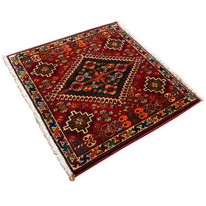 Three-quarter view: carpet with a burgundy background, colorful motifs, and fringes