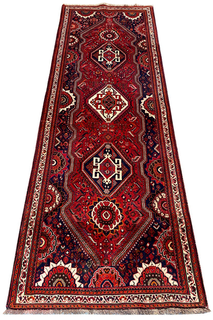 Oriental rug runner with a red background, multiple medallions in white and dark blue, borders