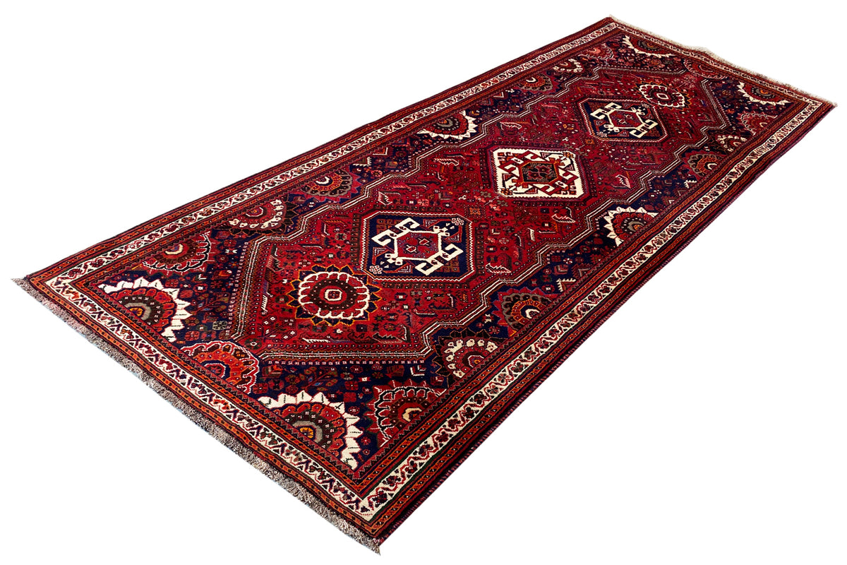 Oriental runner rug, photographed at an angle: red ornamental field, white details, dark blue border