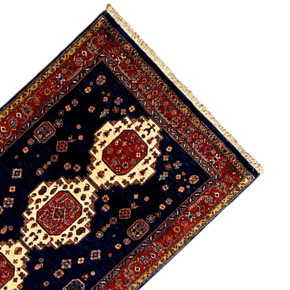 Corner of a dark blue runner rug with a red border and fringe