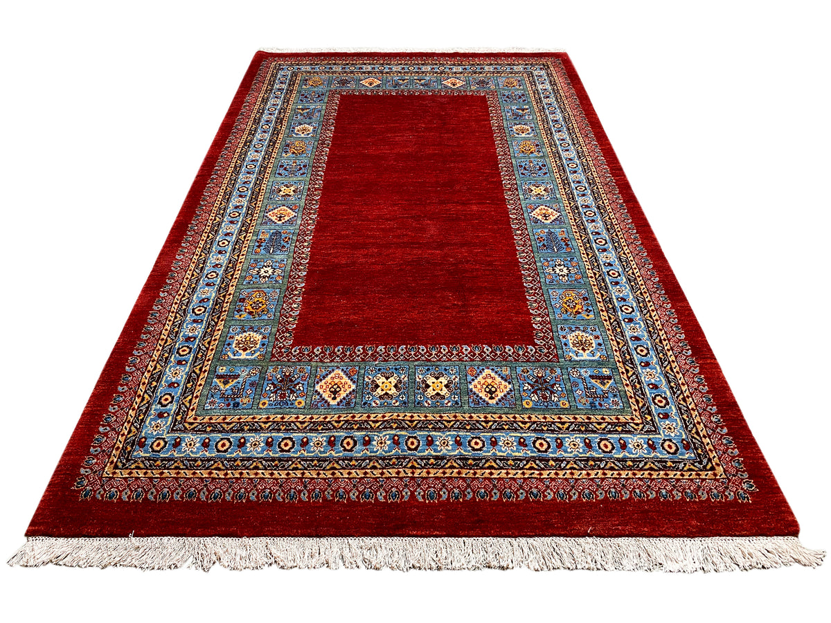 Roter Teppich mit breiter blau verzierter Bordüre und Fransen am Rand.