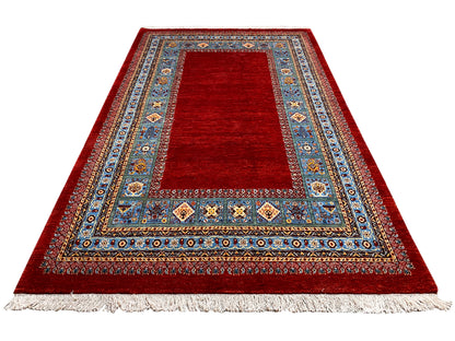 Roter Teppich mit breiter blau verzierter Bordüre und Fransen am Rand.