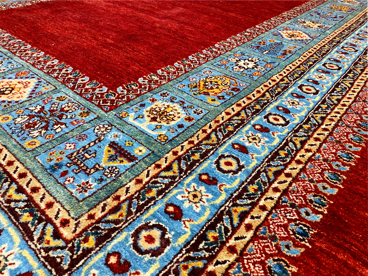 Detailansicht: Blaues Medaillon- und Musterband auf rotem Teppich, mit Bordüre.