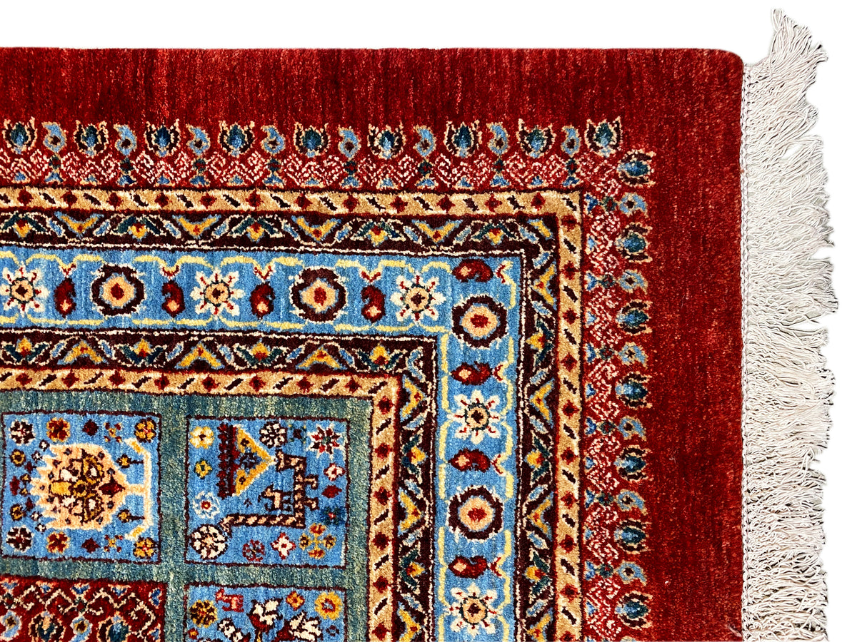 Ecke vom roten Teppich mit blauem Ornamentrahmen und weißen Fransen.