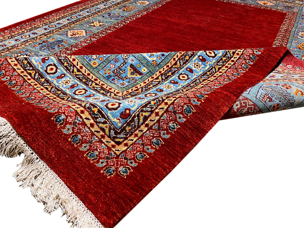Nahansicht der gefalteten Kante: roter Teppich mit blauem Muster und Fransen.