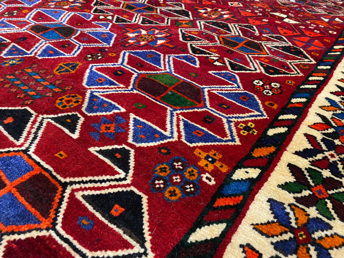 Detailansicht: rotes Teppichgewebe mit großem geometrischem Muster in Blau, Creme und Grün
