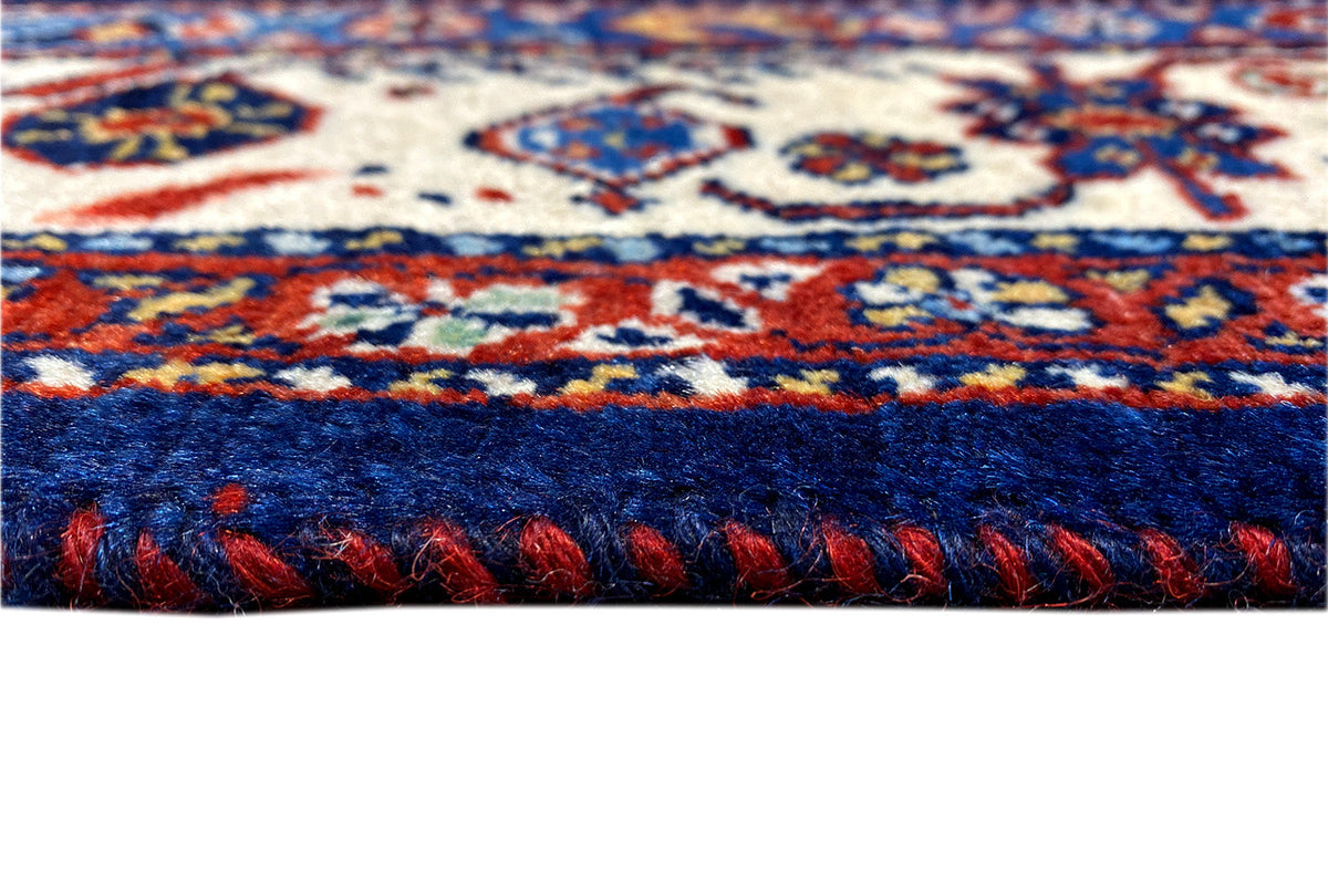 Close-up: blue carpet with a multicolored pattern and a fringed, hemmed edge.