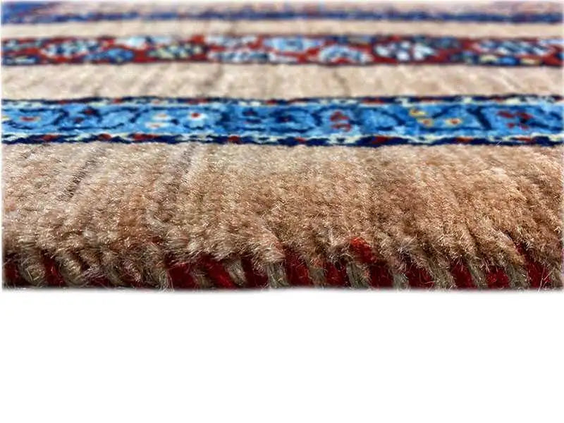 Close-up of a carpet edge with fringes, beige surface and blue patterned stripe