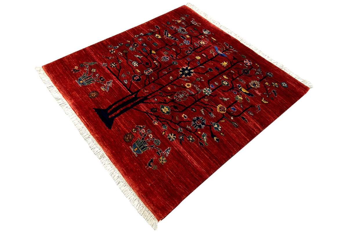 Reddish-brown rug viewed at an angle, tree motif with floral patterns, fringes