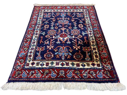 Rug with a blue central motif, red decorative borders, a white edge, and fringes